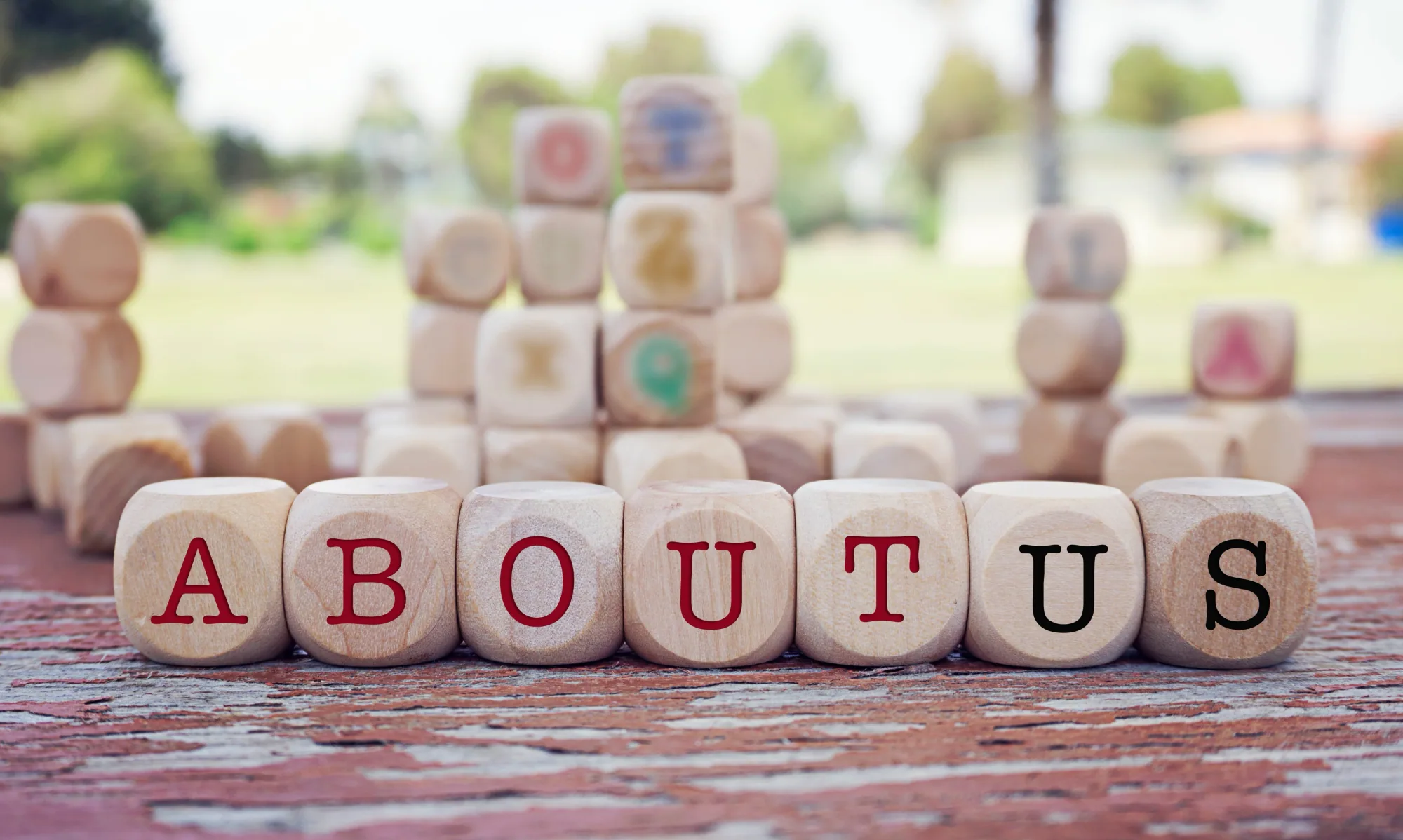Wooden lettered cubes arranged on a weathered surface to spell ‘About Us’, with more blocks stacked behind.