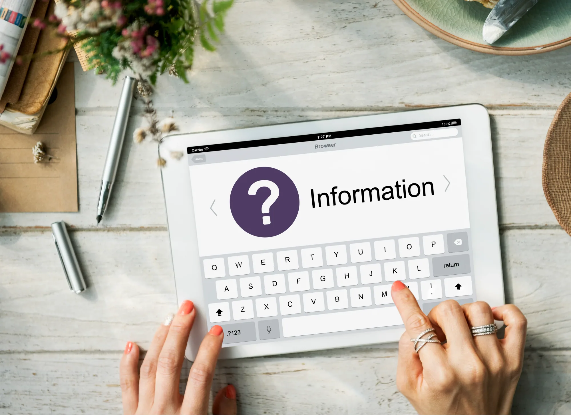 Overhead view of a tablet on a pale wooden desk showing a page headed with a question mark and the word ‘Information’.