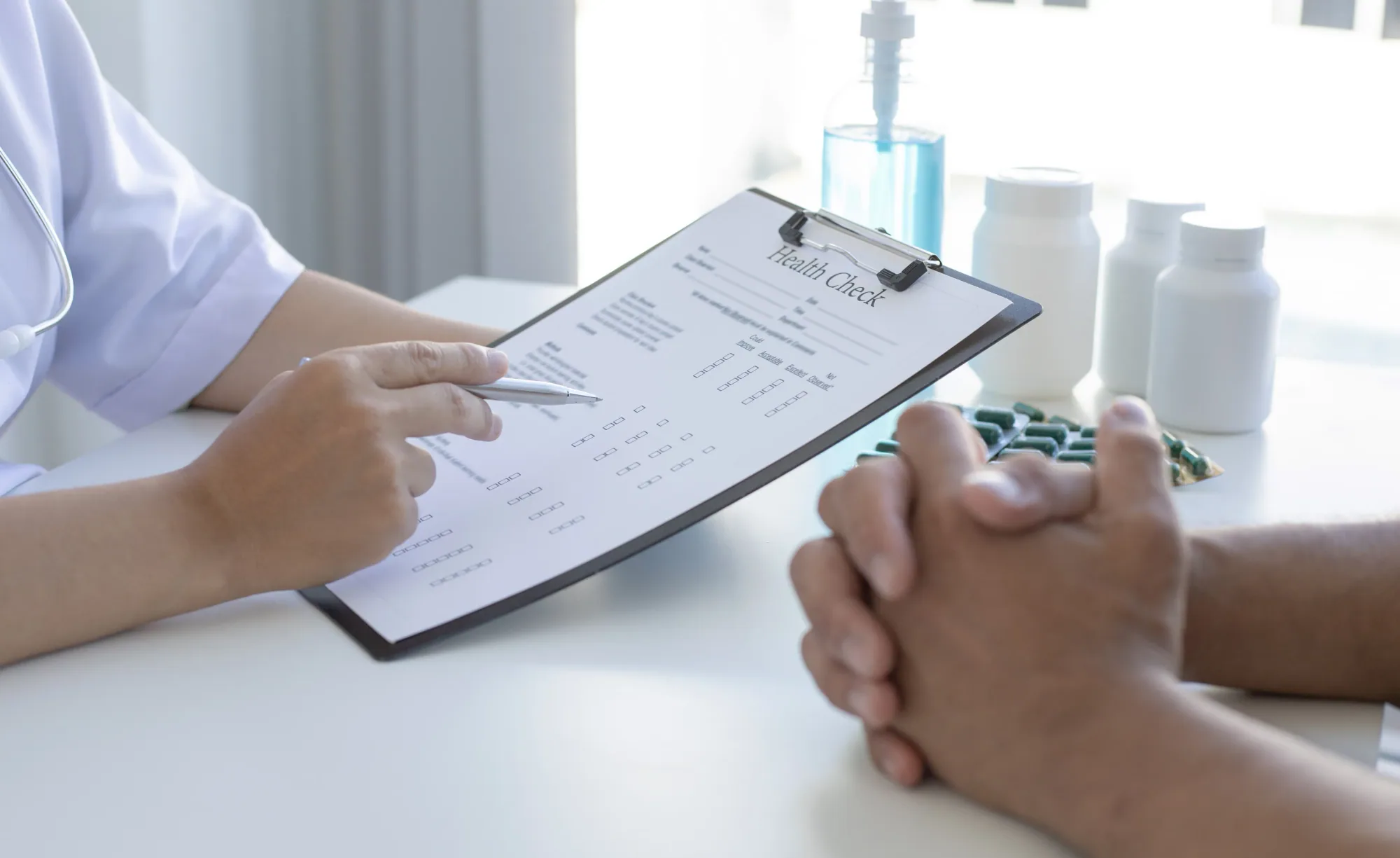 A healthcare professional going through a health check form with a patient, with medication packs on the desk.