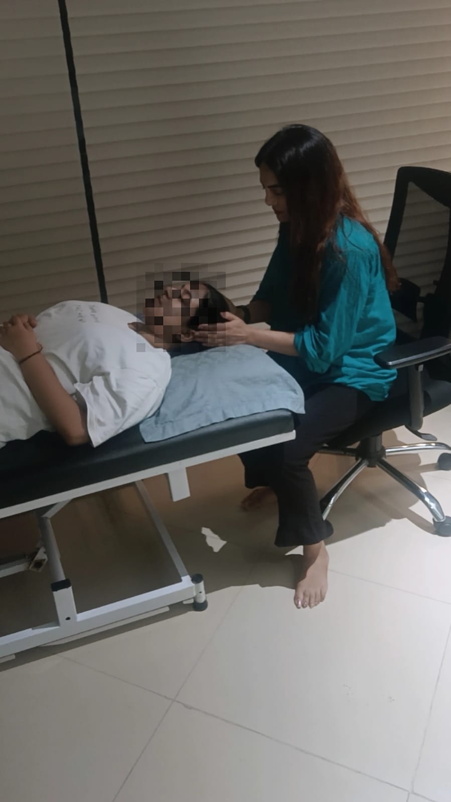 Vibha Jain seated beside a client resting on a treatment couch during a session in a quiet room.