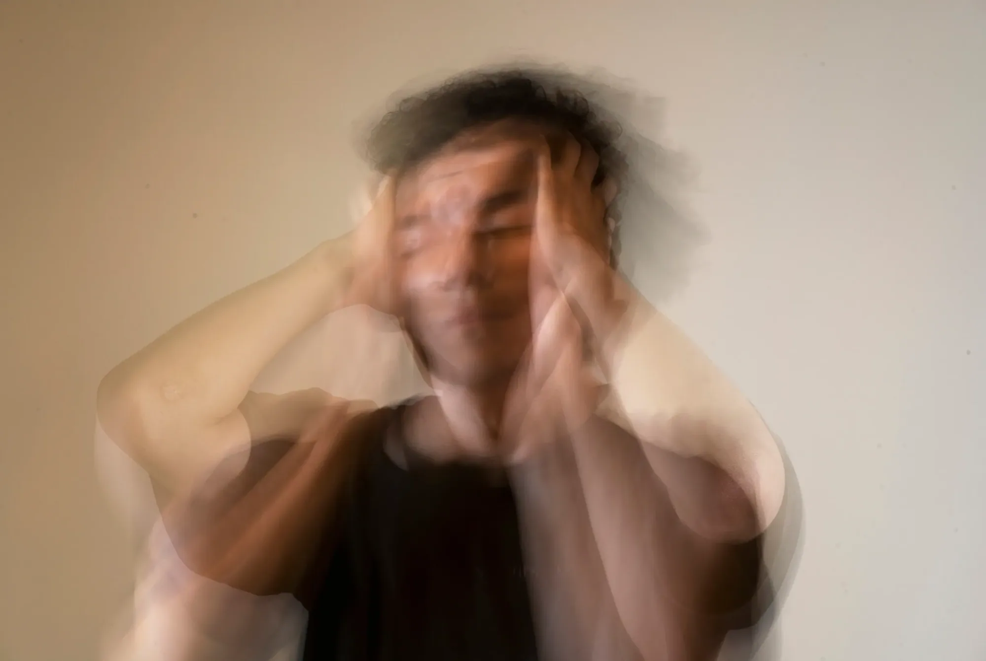 A softly blurred, multiple-exposure portrait of a person with their hands at their head, suggesting movement and change.